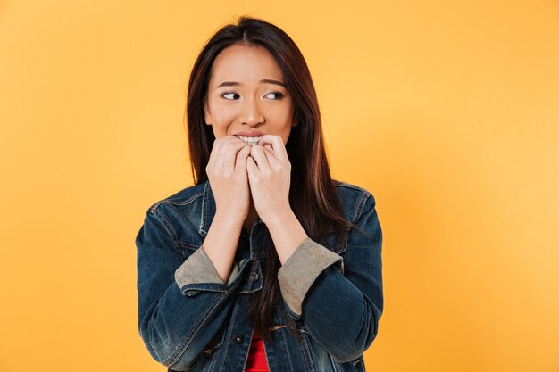 Worried asian woman in jacket bites fingers and looking away