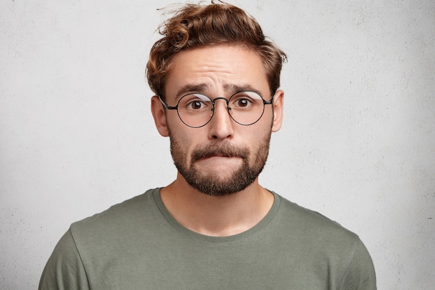 Free Photo worried bearded guy in eyewear, bites lower lip, anticipate important decision or feels nervous