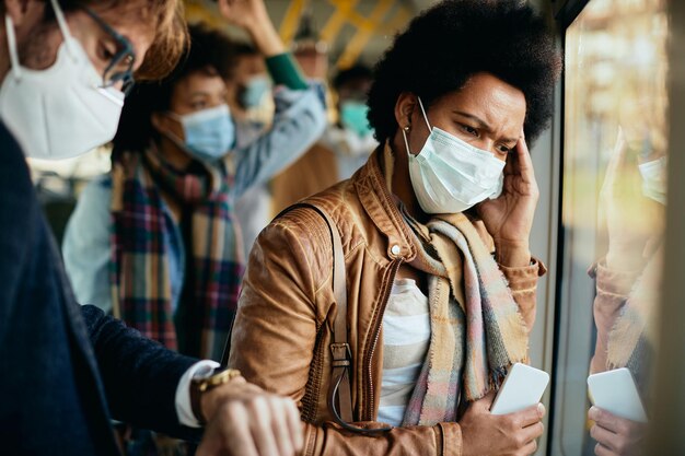 Worried black woman wearing face mask while traveling by public transport during coronavirus pandemic