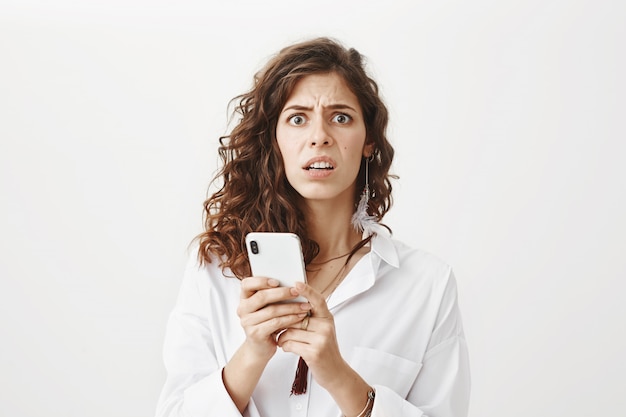 Worried and confused woman reading a strange message on the mobile phone