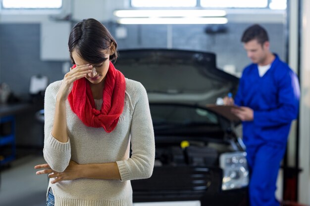 Worried customer standing while mechanic examining car in background