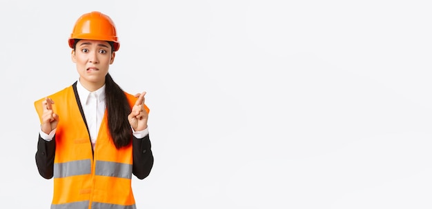 Worried hopeful asian female architect feeling nervous as waiting for inspection results at construction area wearing safety helmet cross fingers good luck hope everything be well