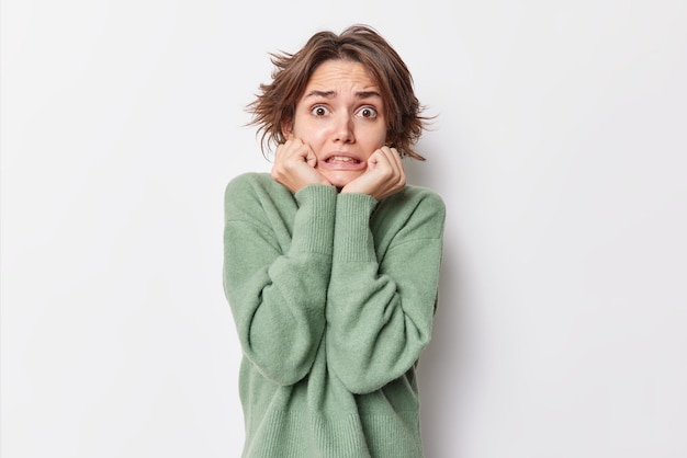 Free Photo worried stressed young woman keeps hands under chin afraids of something wears casual jumper stands embarrassed poses against white background reacts to scary news poses indoor. human reaction