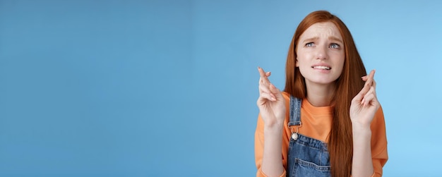 Free photo worried unconfident young redhead intense cute girl frowning nervously waiting improtant moment cross fingers good luck bite lip anxiously frowning look upper left corner praying wish come true