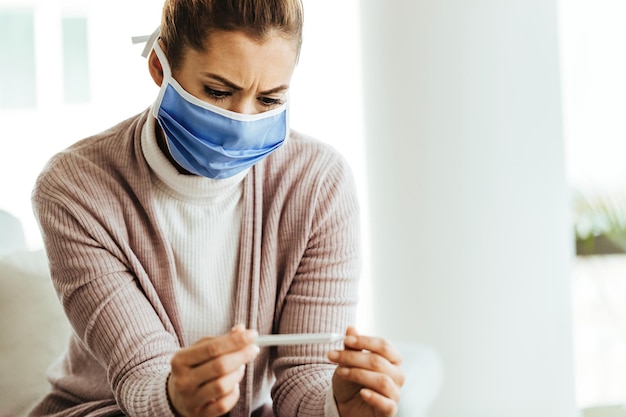 Free Photo worried woman wearing protective face mask and measuring her temperature at home