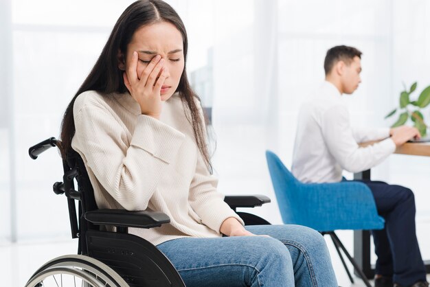 Free photo worried young woman sitting on wheel chair sitting in front of male colleague using laptop