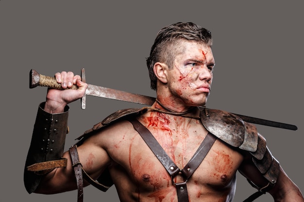 Free Photo wounded gladiator with muscular body holding a sword