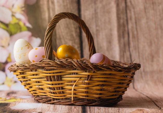 Free photo woven basket filled with colorful easter eggs on a wooden surface decorated with artificial foliage