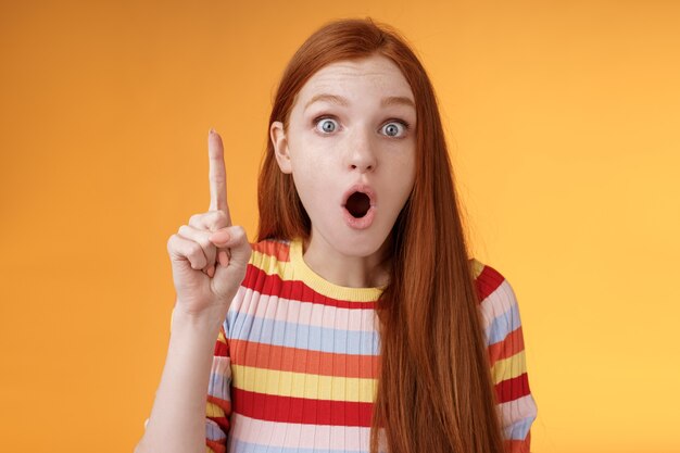 Wow got excellent idea. Excited shocked redhead girl open mouth raise index finger eureka gesture stare camera thrilled adding suggestion have plan think-up solution, standing orange background.