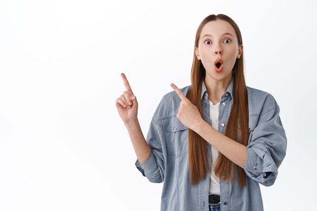 Free Photo wow look this way impressed teen girl gasping pointing aside at banner with awesome promo deal showing special offer display banner copyspace standing over white background