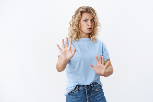 Wow slow down Intense and concerned woman breathing heavy raising hands in defense and no gesture folding lips alarmed step back as refusing and trying calm person acting crazy over white wall