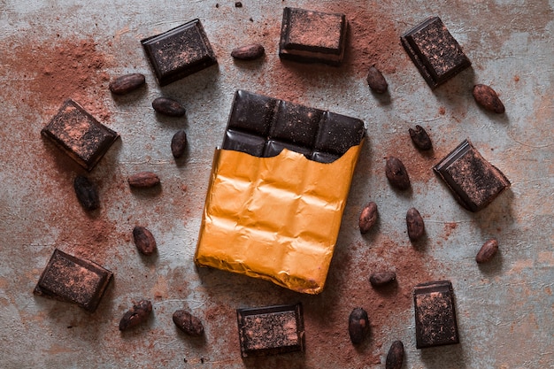 Free photo wrapped chocolate bar and cocoa beans on rustic background