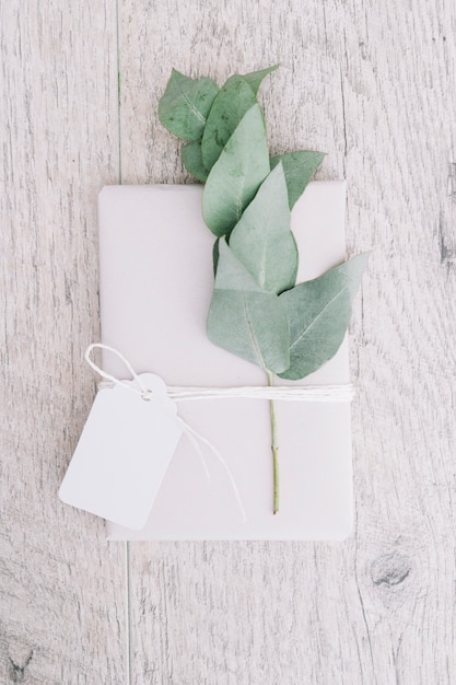 Free Photo wrapped white present with blank tag and twig on wooden background