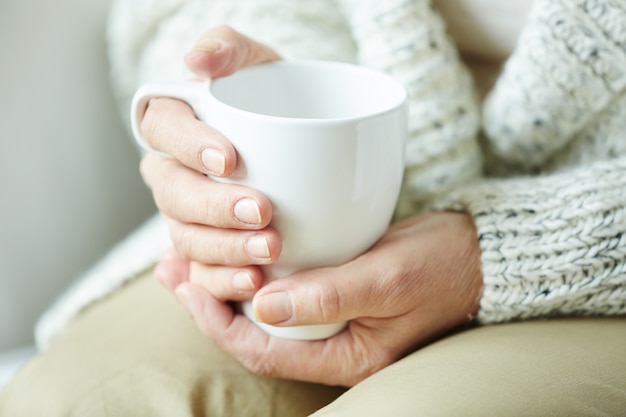 Wrinkled female hands holding cup of coffee