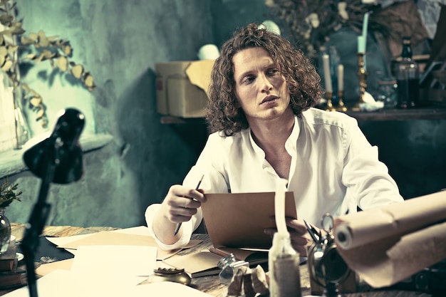 Writer at work. Handsome young writer sitting at the table and writing something in his sketchpad at home