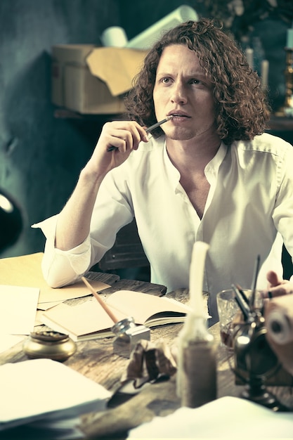 Writer at work. Handsome young writer sitting at the table and writing something in his sketchpad at home