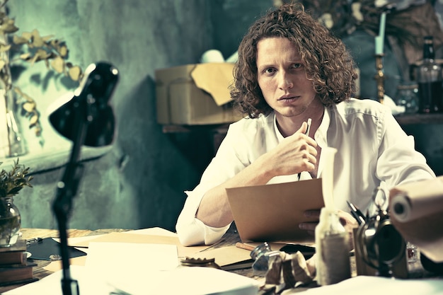 Writer at work. Handsome young writer sitting at the table and writing something in his sketchpad