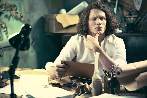 Writer at work. Handsome young writer sitting at the table and writing something in his sketchpad