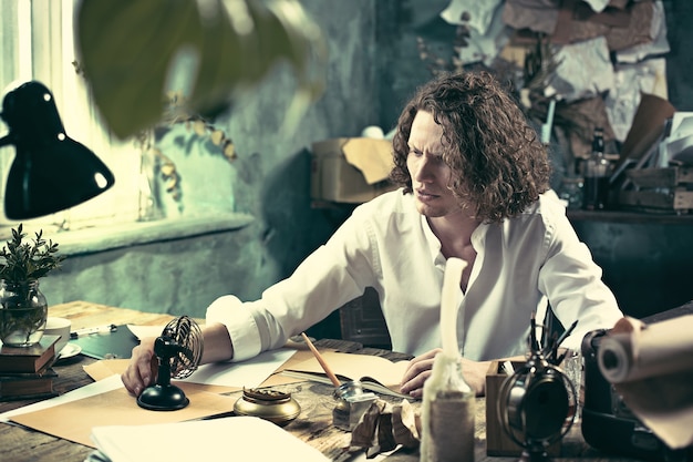 Writer at work. Handsome young writer sitting at the table and writing something in his sketchpad