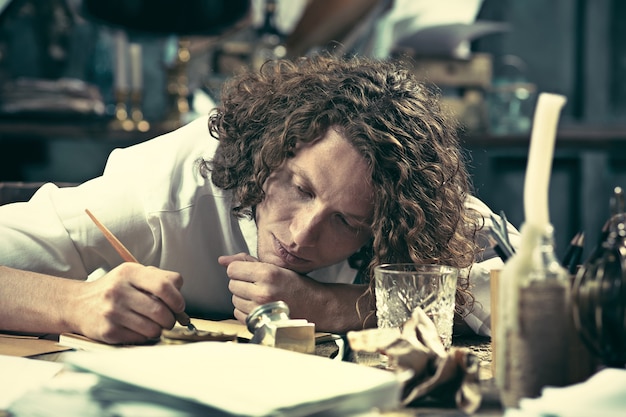 Free photo writer at work. handsome young writer sitting at the table and writing something in his sketchpad