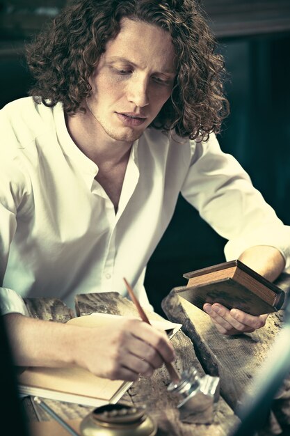 Writer at work. Handsome young writer sitting at the table and writing something in his sketchpad