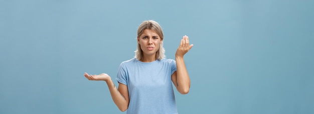 Free Photo wtf you saying portrait of pissed and confused stylish girlfriend with blond hair raising palm high and aside with perplexed expression being questioned hearing stupid nonsense over blue wall