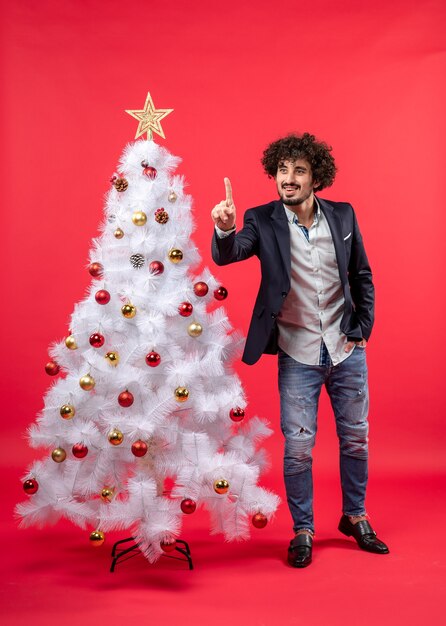 xmas celebration with bearded young man showing one and standing near Christmas tree