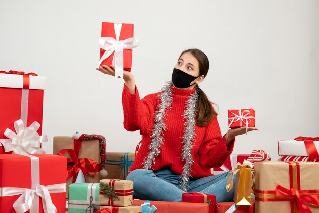 Free photo xmas girl with black mask holding gifts in both hands sitting around presents on white