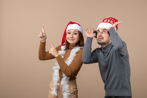 Free photo xmas mood with excited cool satisfied lovely couple wearing red santa claus hats pointing above