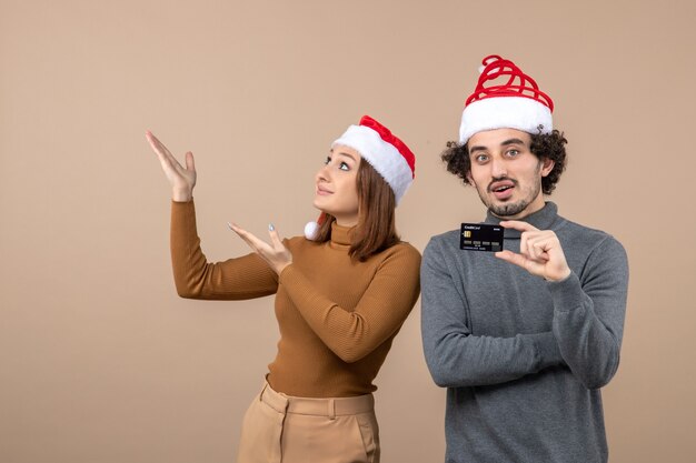 Free photo xmas mood with excited happy cool couple wearing red santa claus hats showing bank card