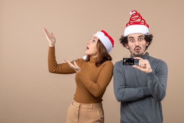 xmas mood with excited satisfied shocked cool couple wearing red santa claus hats showing bank card