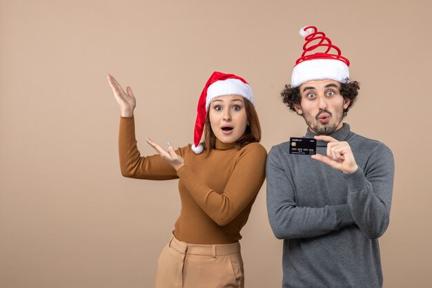 xmas mood with excited satisfied surprised cool couple wearing red santa claus hats showing bank card