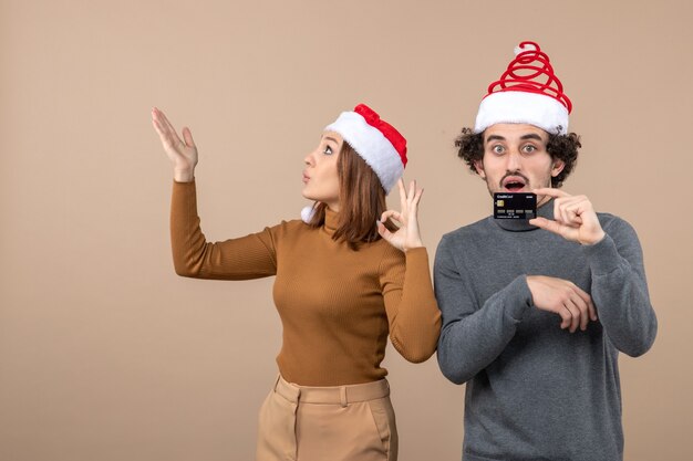 xmas mood with excited satisfied surprised cool couple wearing red santa claus hats showing bank card