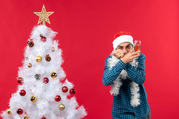 xmas mood with happy crazy emotional young man with santa claus hat in a blue stripped shirt raising a glass of wine near Christmas tree