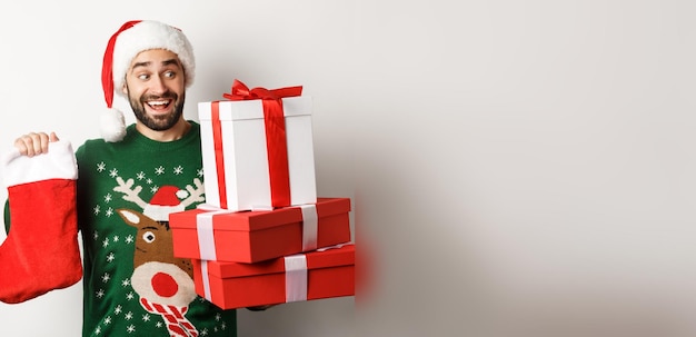 Free Photo xmas and winter holidays concept excited man holding christmas sock and gift boxes celebrating new y