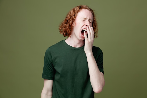 Free Photo yawning covered mouth with hand young handsome guy wearing green t shirt isolated on green background