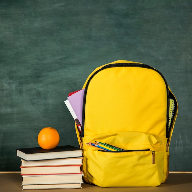 Free Photo yellow backpack, stack of books and orange