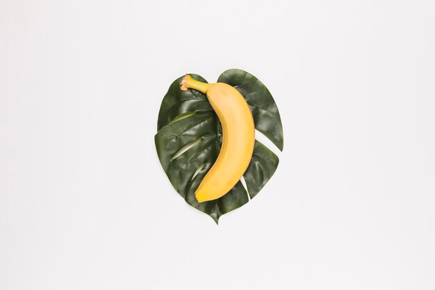 Yellow banana on green leaf in center of white surface