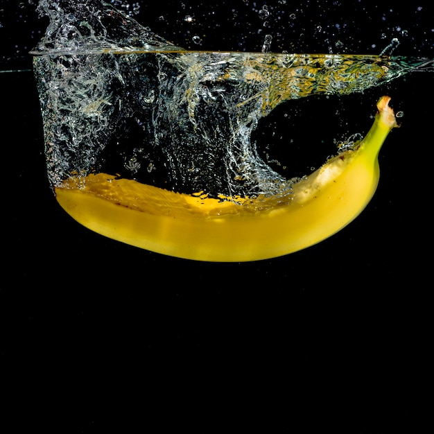 Free Photo yellow banana splashing into water against black background