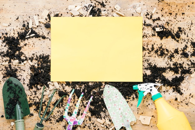 Yellow blank empty paper over soil with gardening equipments