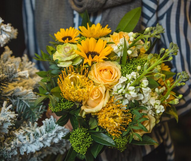 A yellow bouquet of sunflowers and roses in the hands of a dame