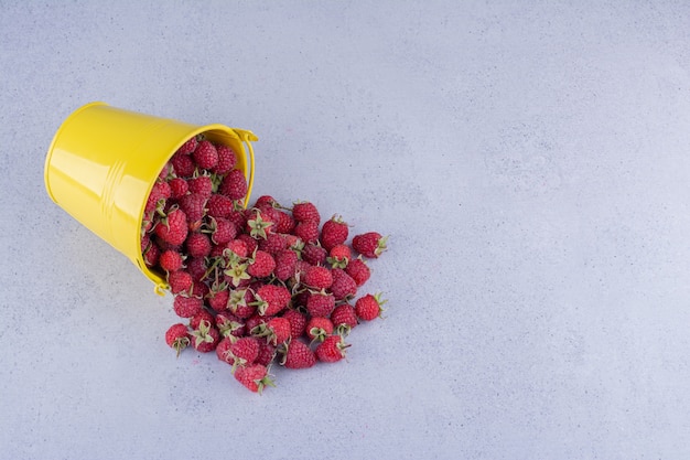 Free Photo yellow bucket of raspberries spilled over on marble background. high quality photo