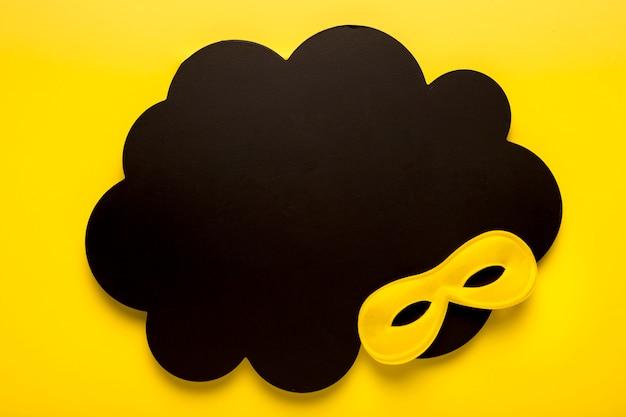 Free photo yellow carnival mask on black paper cloud