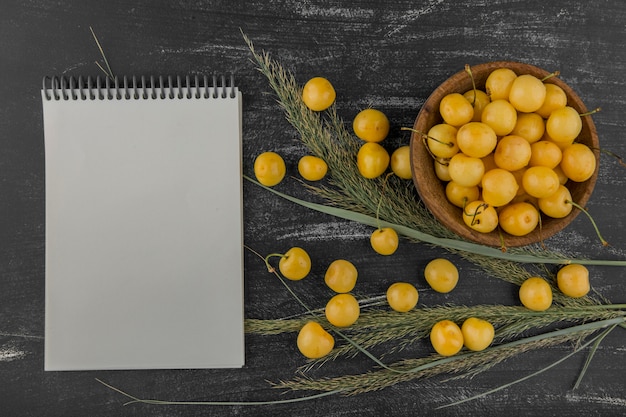 Yellow cherries in a wooden bowl with a notebook aside