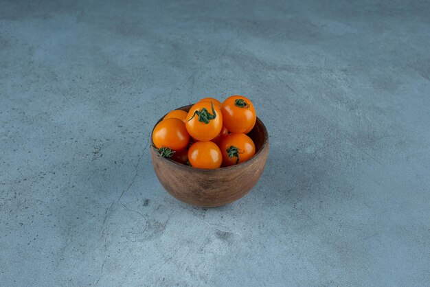 Yellow cherry tomatoes in a cup on blue.