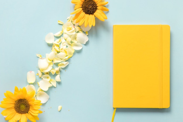 Free photo yellow diary near sunflowers and petals over blue background