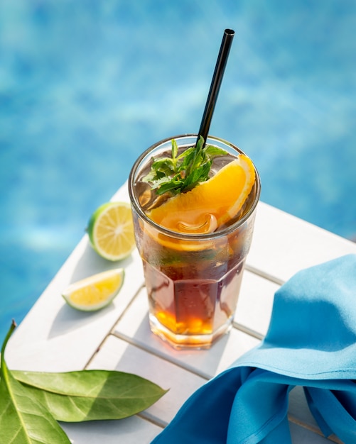 Yellow drink with orange,lemon and mint leaves by the pool.