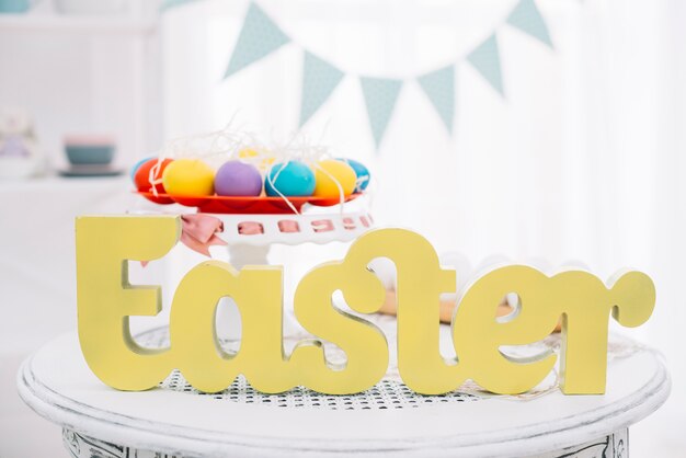 Yellow easter text in front of colorful easter eggs on cakestand