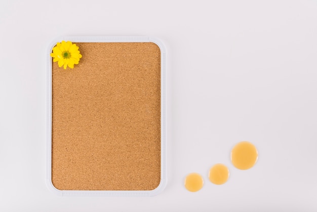 Yellow flower on cork frame near honey drops over white background