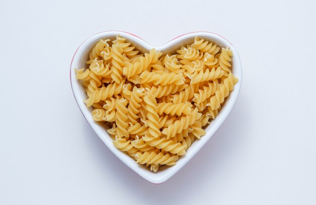 Free Photo yellow fusilli pasta in a heart shaped bowl on a white table. flat lay.